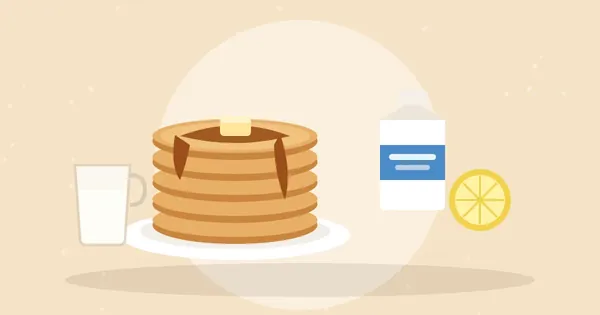Stack of fluffy pancakes with butter and syrup next to a buttermilk carton, lemon half and measuring cup of milk