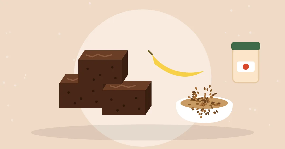 Squares of fudgy chocolate brownies next to a bowl of flax seeds, a ripe banana and a jar of applesauce